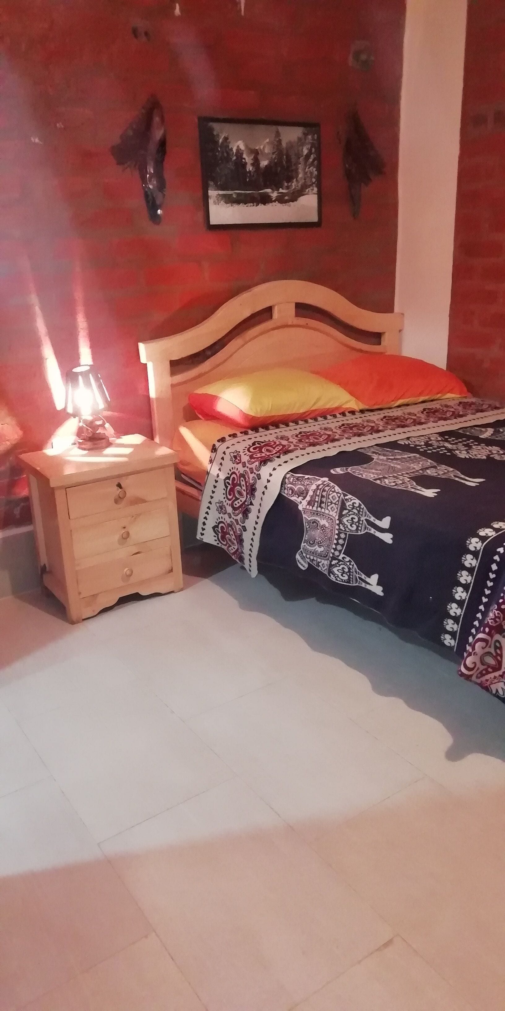 Ein Schlafzimmer mit einem hölzernen Bett, einem Nachttisch mit Lampe sowie einem gerahmten Bild an der Wand.