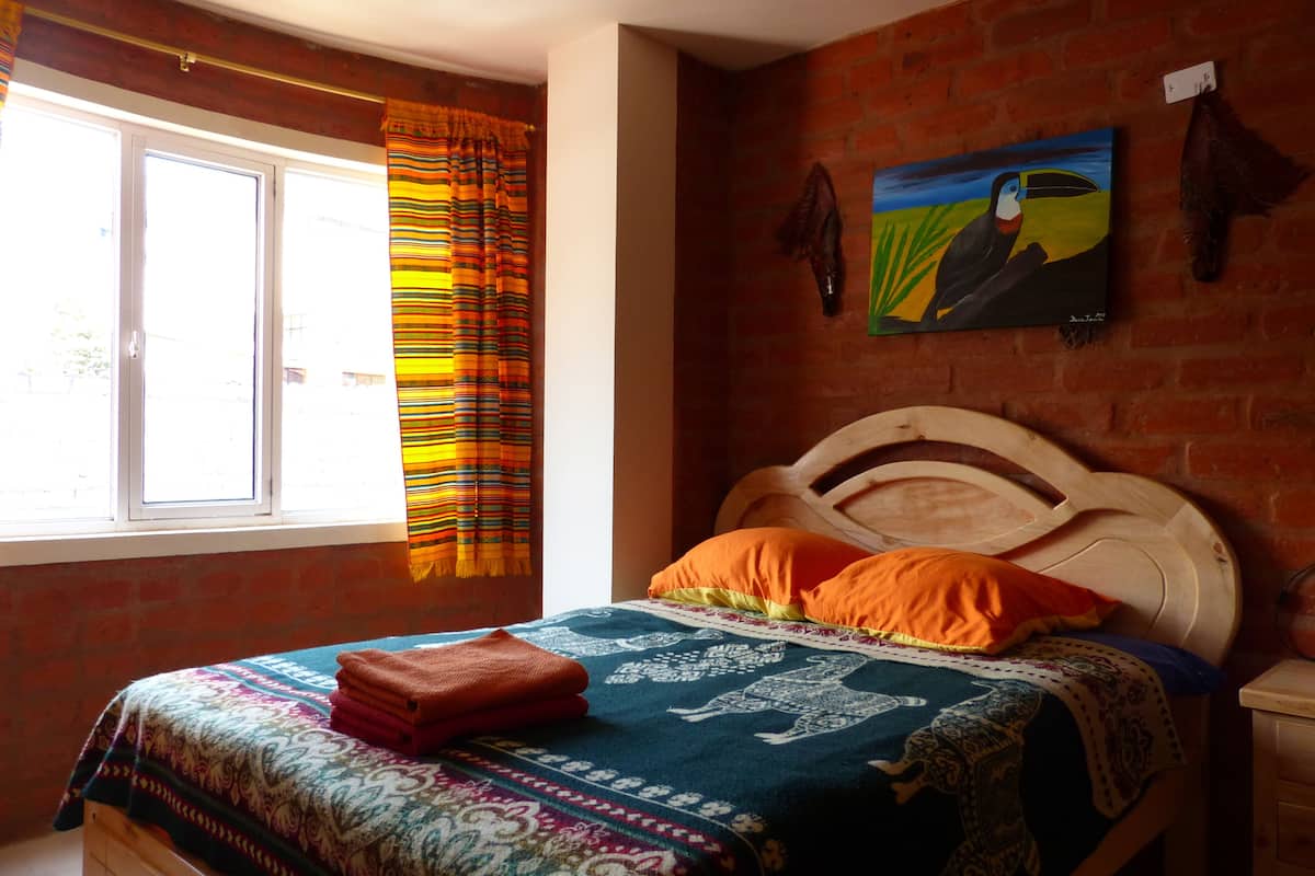 A bedroom with a wooden bed, colorful curtains, a painting, and a brick wall.