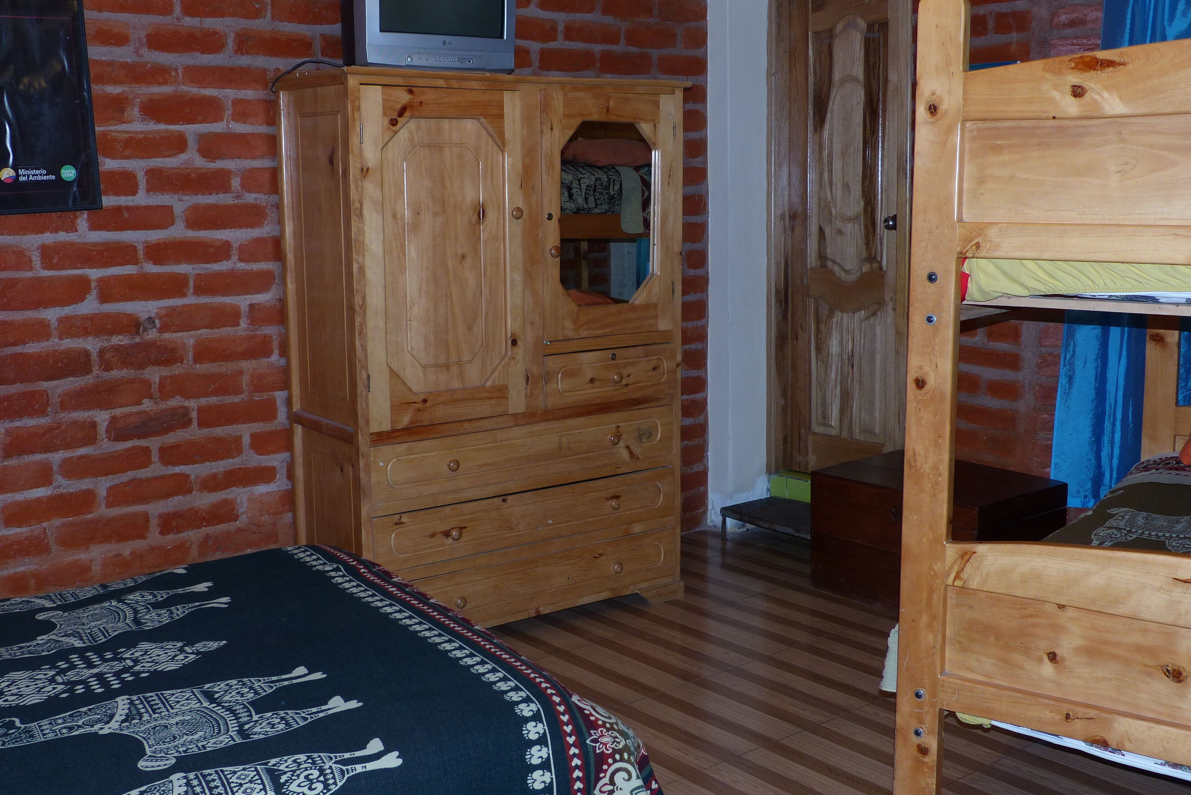 A room with a wooden wardrobe, a bed with patterned bedding, and a bunk bed.