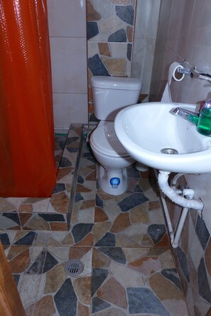 A bathroom with a toilet, sink, and a shower curtain. - Hotel La Casa Amarilla City (Baños de Agua Santa)