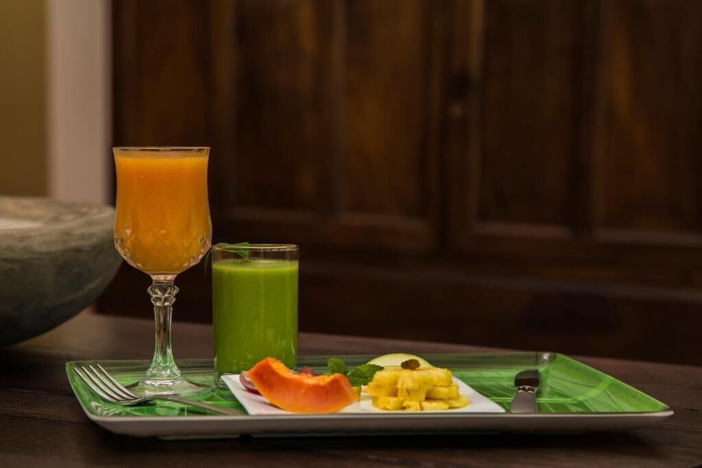 Une assiette de petit-déjeuner avec un verre de jus d’orange, un smoothie vert et une variété de fruits, le tout posé sur un set de table vert.