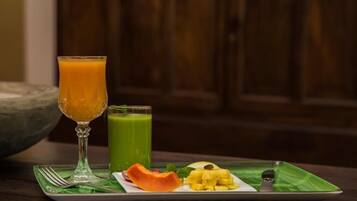Une assiette de petit-déjeuner avec un verre de jus d’orange, un smoothie vert et une variété de fruits, le tout posé sur un set de table vert.
