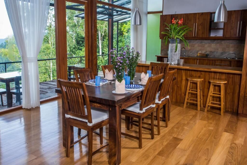 A dining area with a wooden table and chairs, a vase with flowers, and a view of the outdoors.