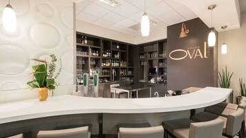 Uma área de bar moderna com balcão curvo, banquetas e prateleiras cheias de garrafas e copos.
