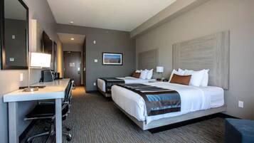 A hotel room with a desk, two beds, a large mirror, and a framed picture on the wall.