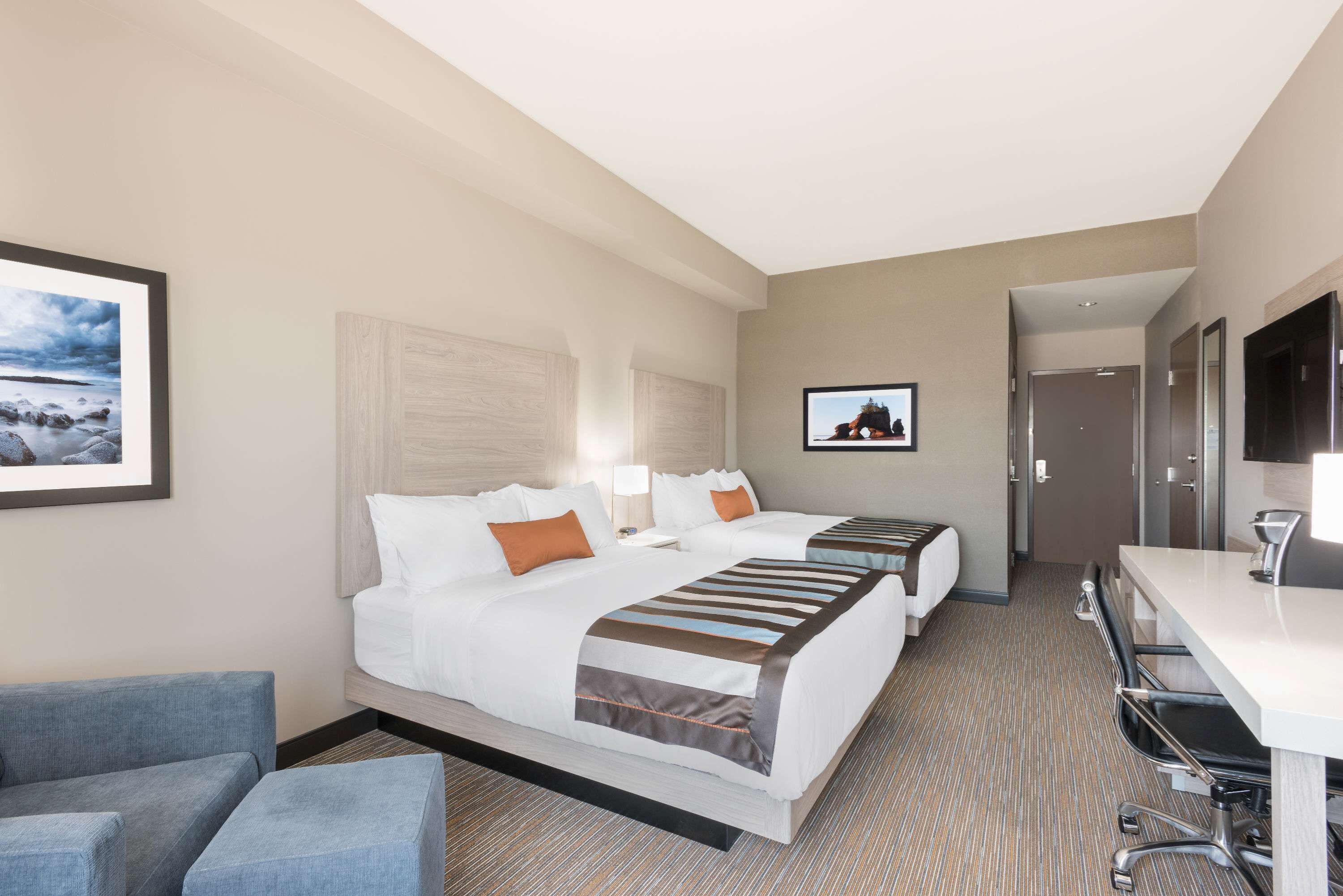 A hotel room with two beds, a desk, a chair, and a TV.