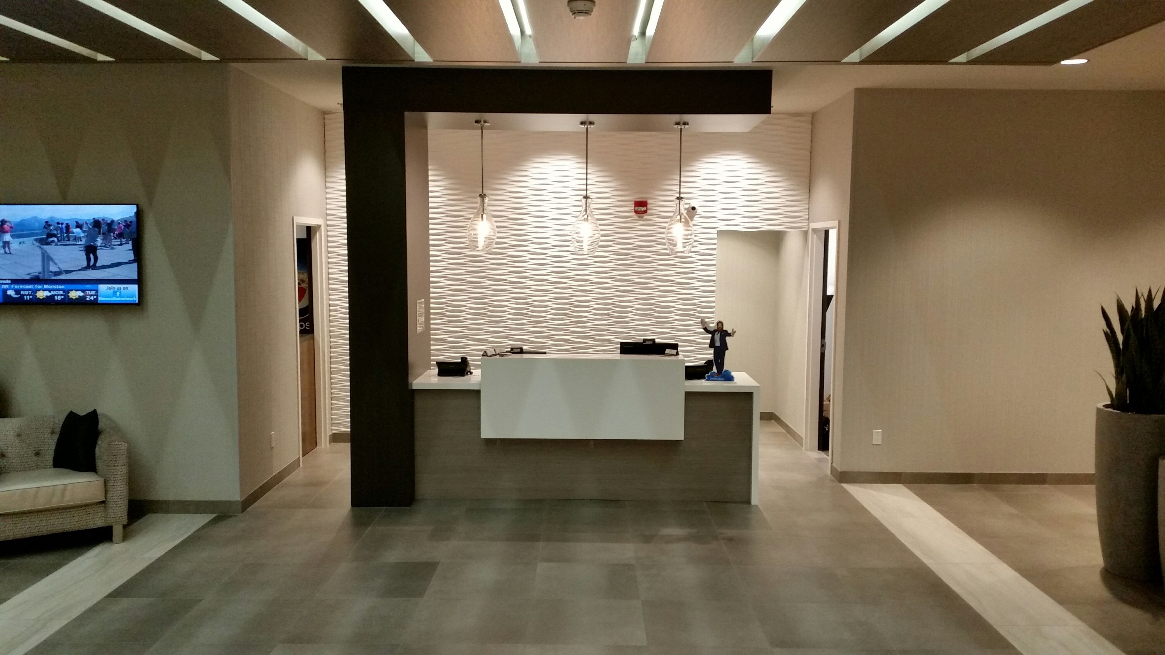 Een receptiezone met een receptiebalie, een wandgemonteerde flatscreen-tv en een gestructureerd wandontwerp.