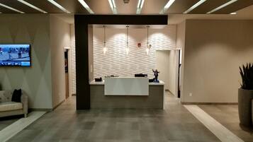 Een receptiezone met een receptiebalie, een wandgemonteerde flatscreen-tv en een gestructureerd wandontwerp.