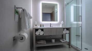 Een moderne badkamer met een douchecabine van glas, een wastafel met spiegel en een toiletrolhouder.