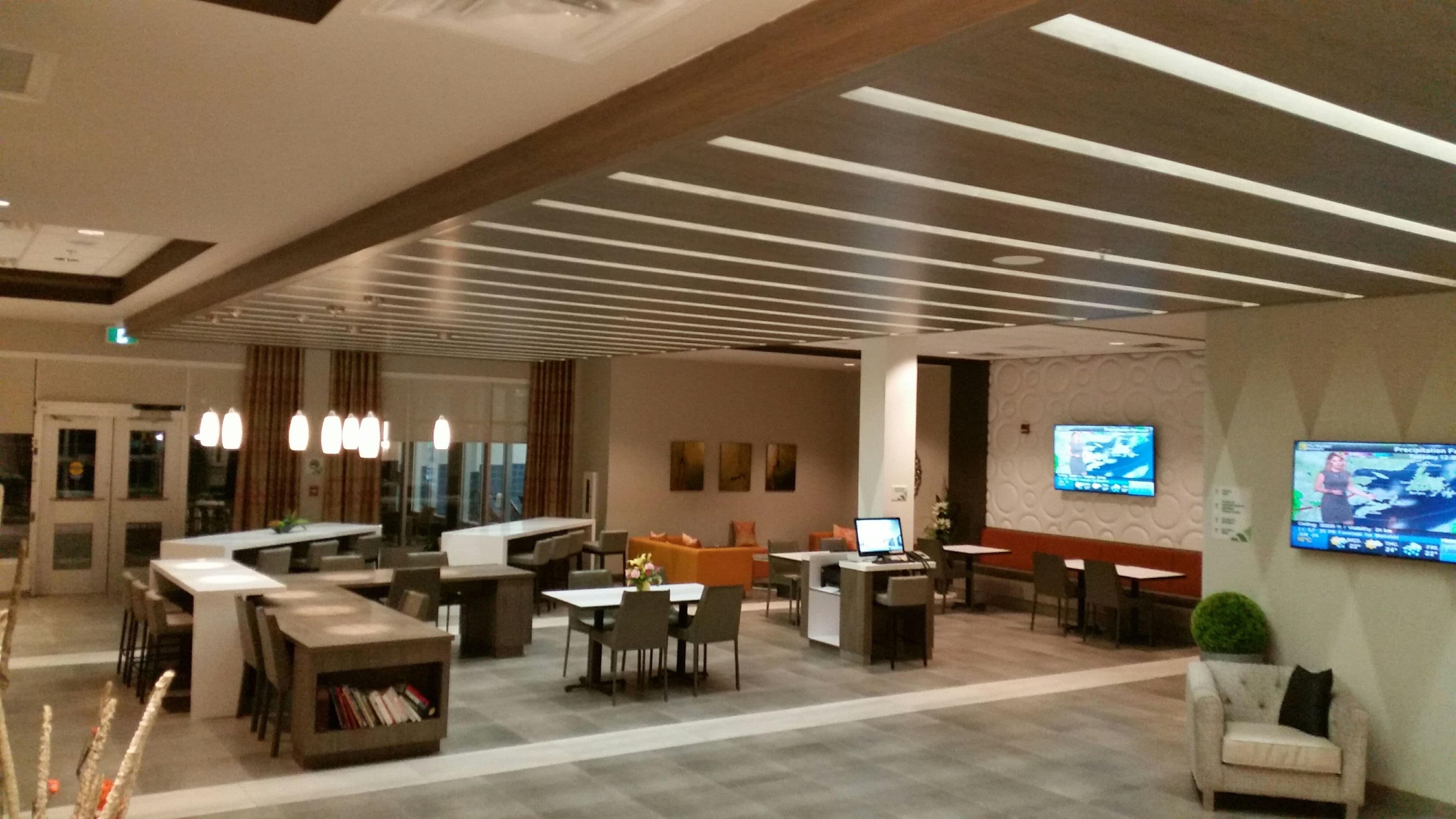 Un lobby moderno con una recepción, zona de estar y un televisor que muestra información meteorológica.