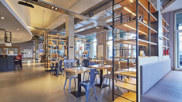 A modern library with bookshelves, tables, and chairs. - Campanile PRIME - Paris Saclay (Gif-sur-Yvette)