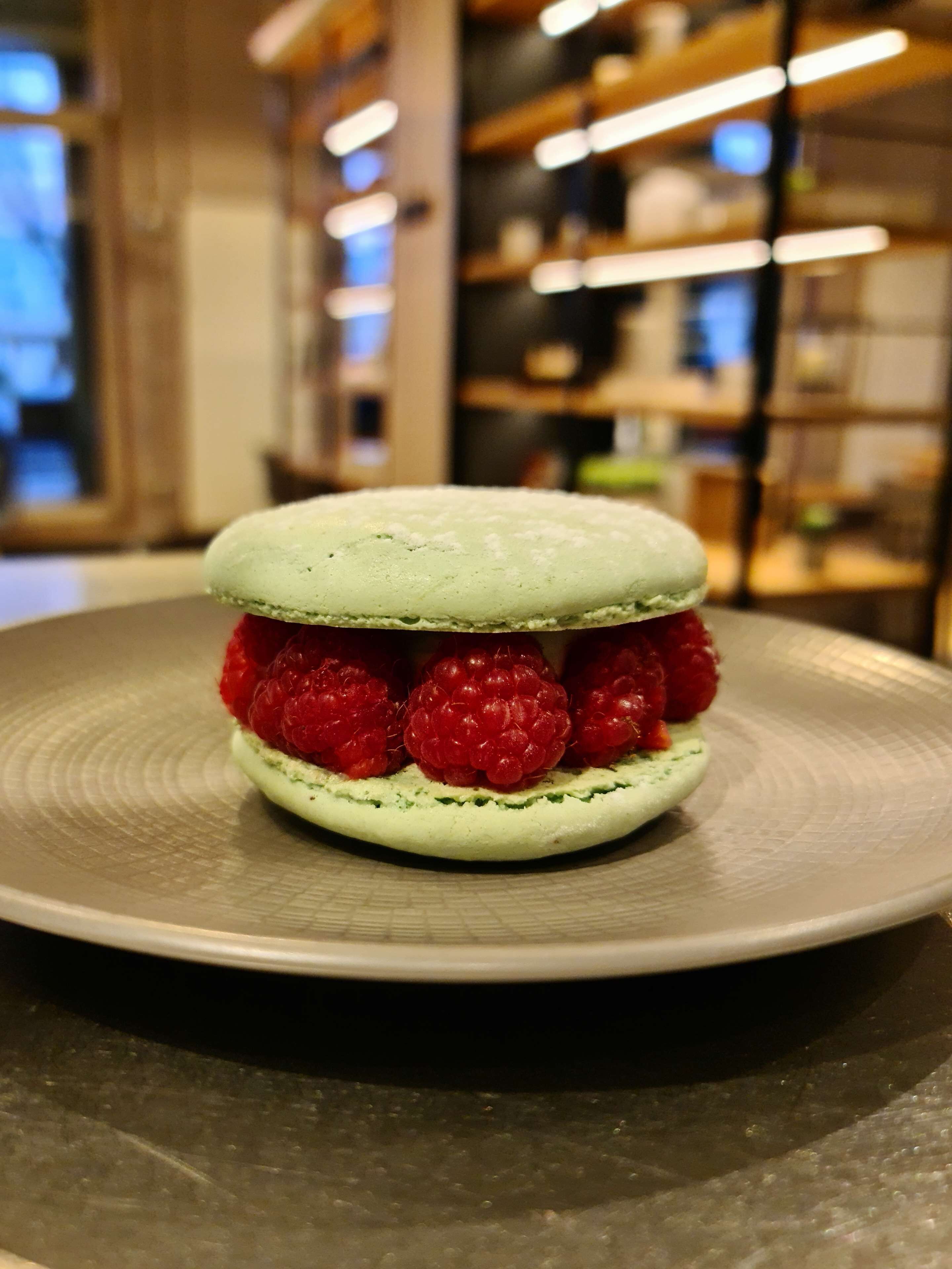 Een dessert met een groene macaron en frambozen op een bord.