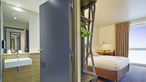 A hotel room with a bed, a bathroom with a sink, and a large mirror. - Campanile PRIME - Paris Saclay (Gif-sur-Yvette)