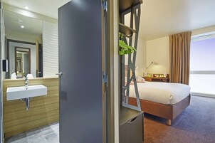 Una habitación de hotel con una cama, un baño con lavamanos y un espejo grande.