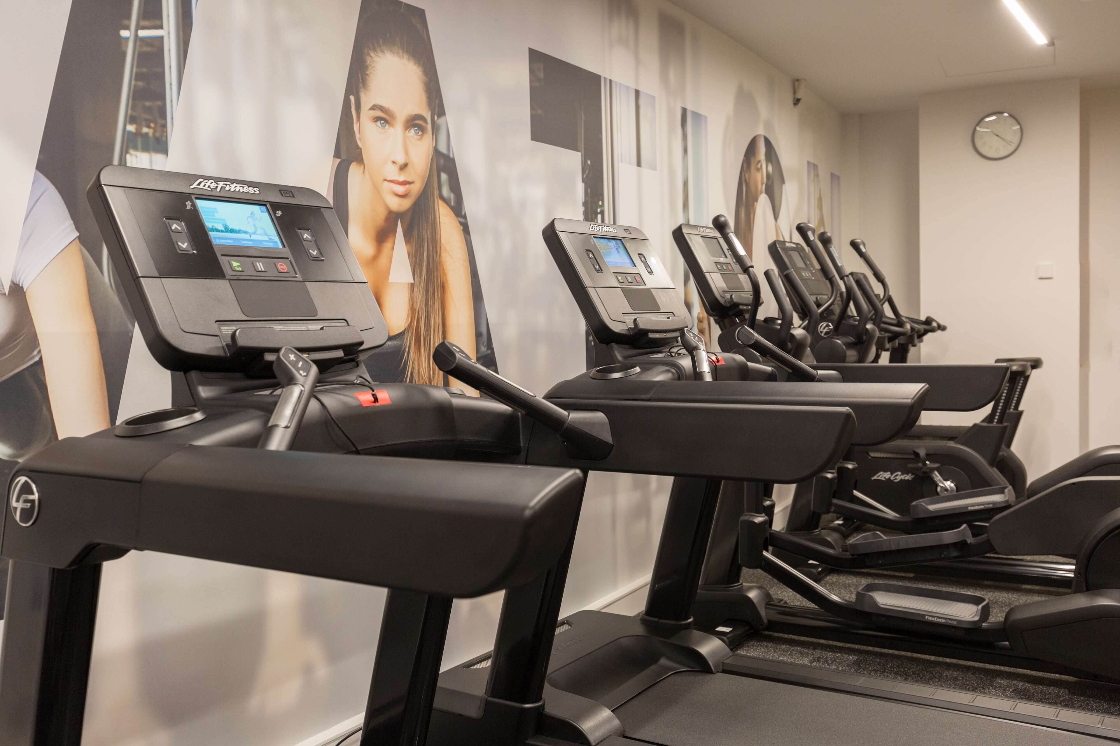 A row of treadmills in a gym with a large poster of a woman on the wall behind them.