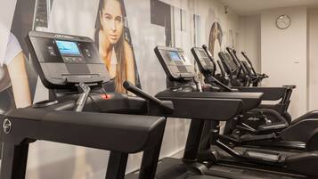 A row of treadmills in a gym with a large poster of a woman on the wall behind them.