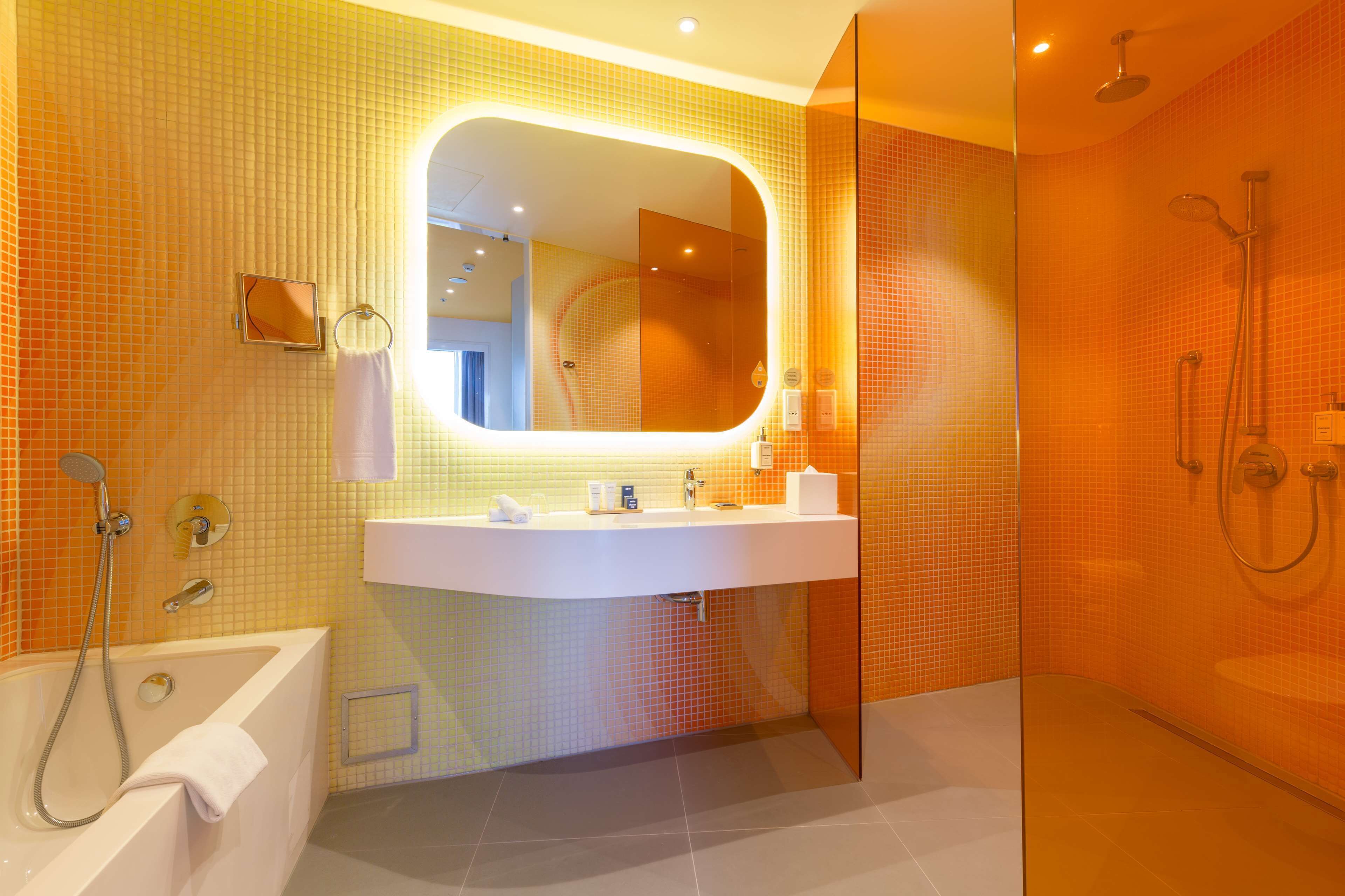A modern bathroom with a large mirror, a bathtub, a shower area, and a sink.