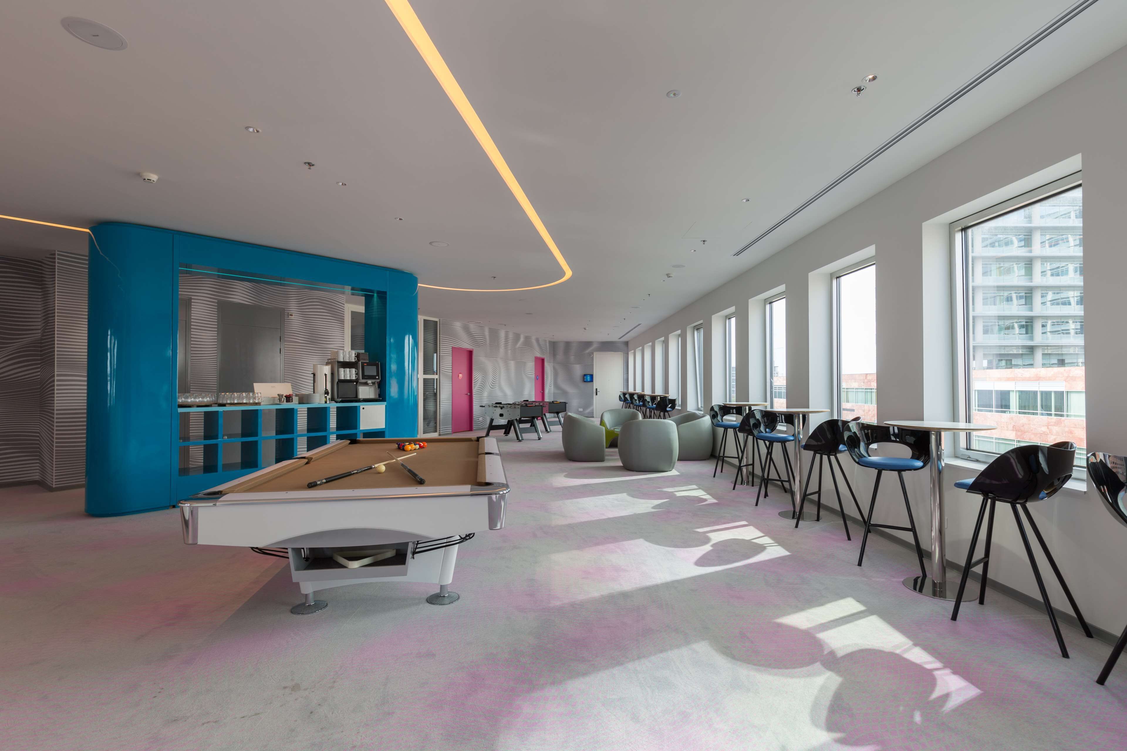 Un'area lounge moderna con tavolo da biliardo, posti a sedere e ampie finestre.