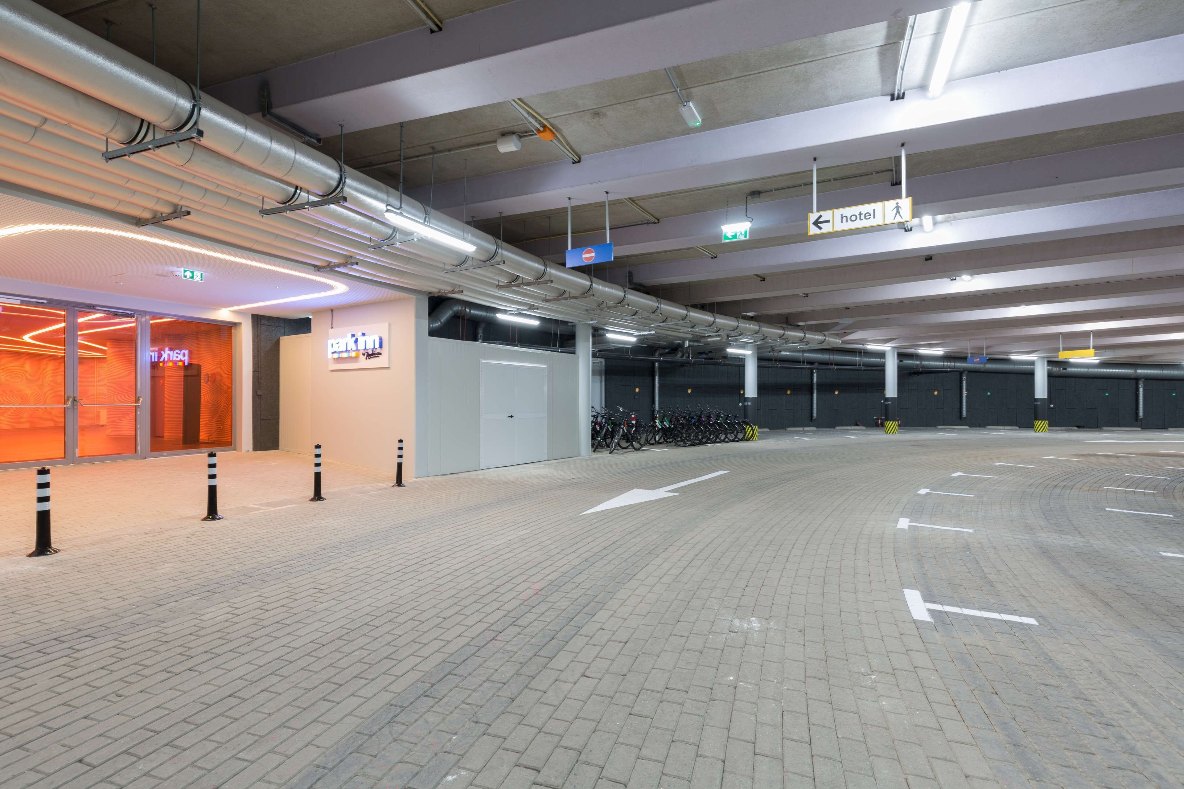 Een ruime parkeergarage met duidelijke routeaanduidingen, een hotelsign en een fietsenstallingsplaats.
