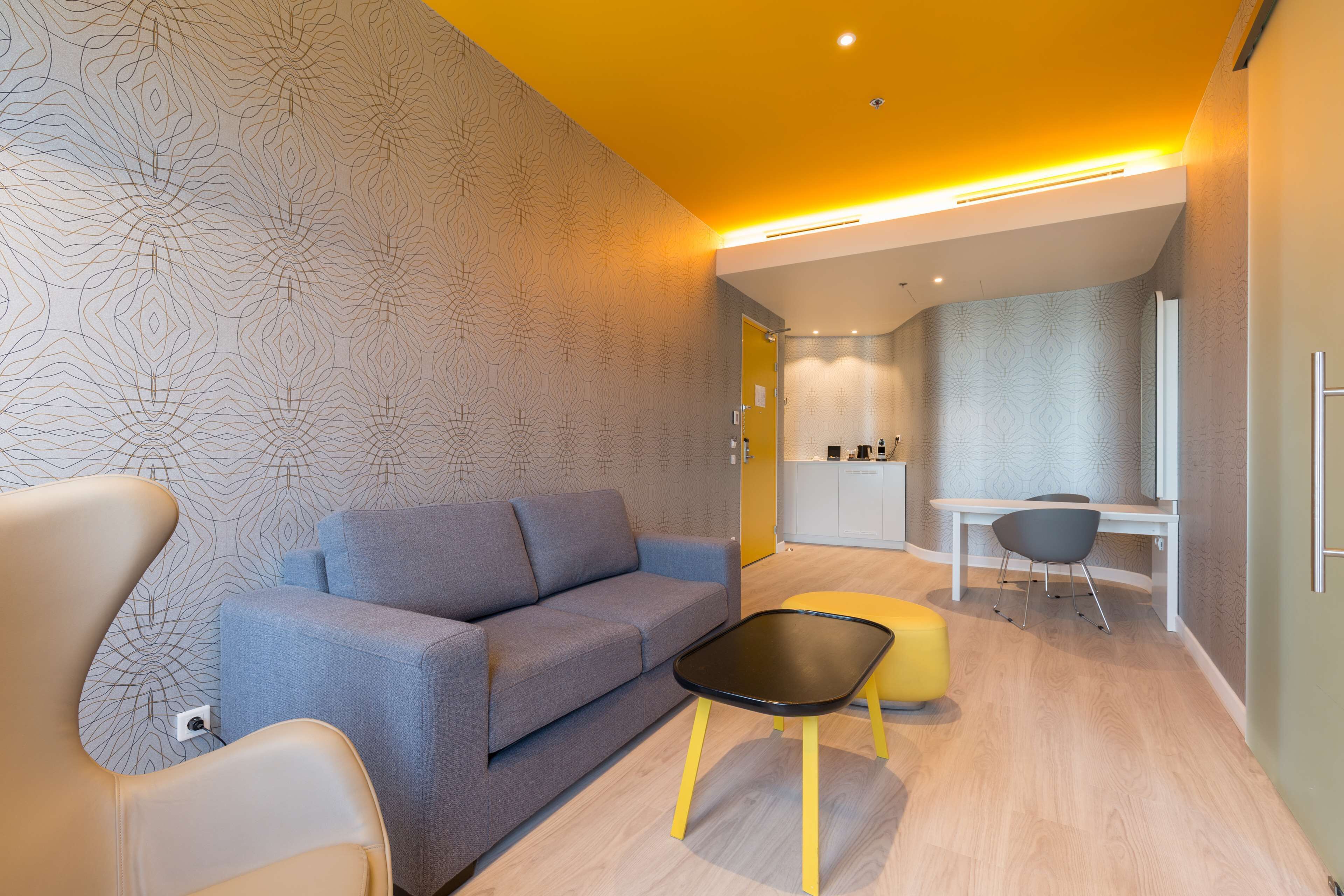 Een moderne woonkamer met een grijze bank, een geel poefje en een zwarte salontafel.