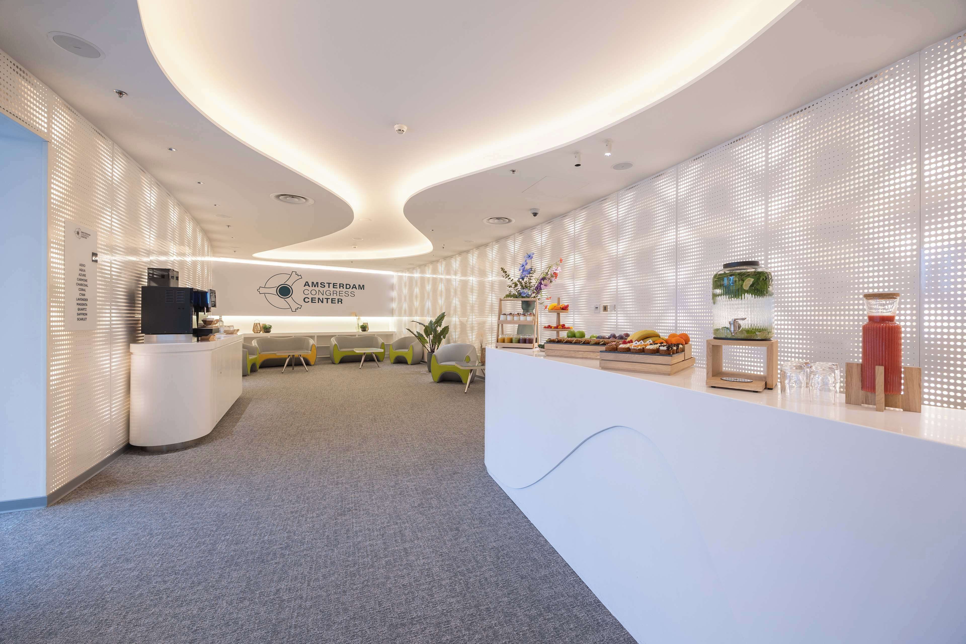 Una zona de recepción moderna con un mostrador blanco curvo, un área de descanso con sillas verdes y un cartel en la pared que dice "AMSTERDAM CONGRESS CENTER".