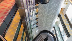 Un interior moderno con una escalera espiral, barandillas de cristal y un papel tapiz estampado.