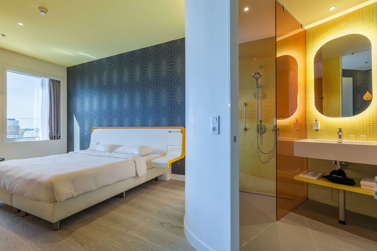 A modern hotel room with a large bed, a shower area, and a bathroom with a mirror and sink.