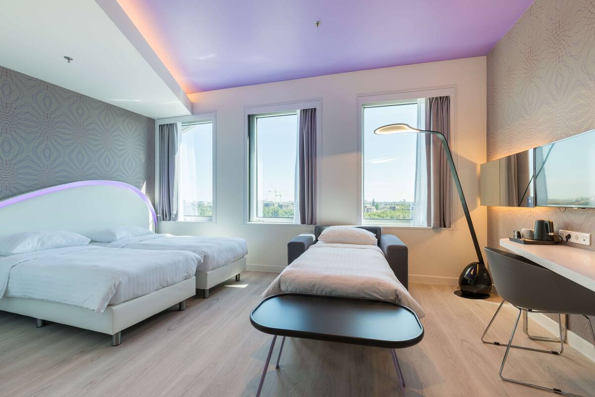 A modern hotel room with two beds, a desk, and a large window.