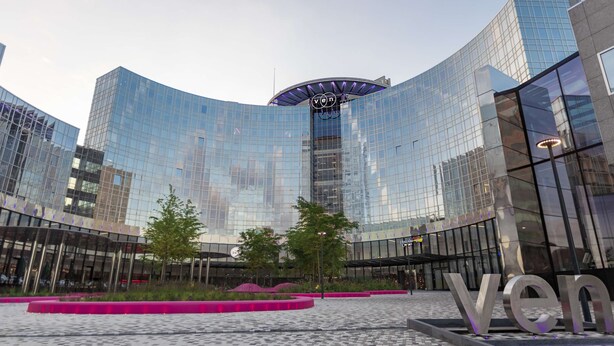 Un edificio moderno con fachada de vidrio curva y la palabra "Ven" visible en el suelo.
