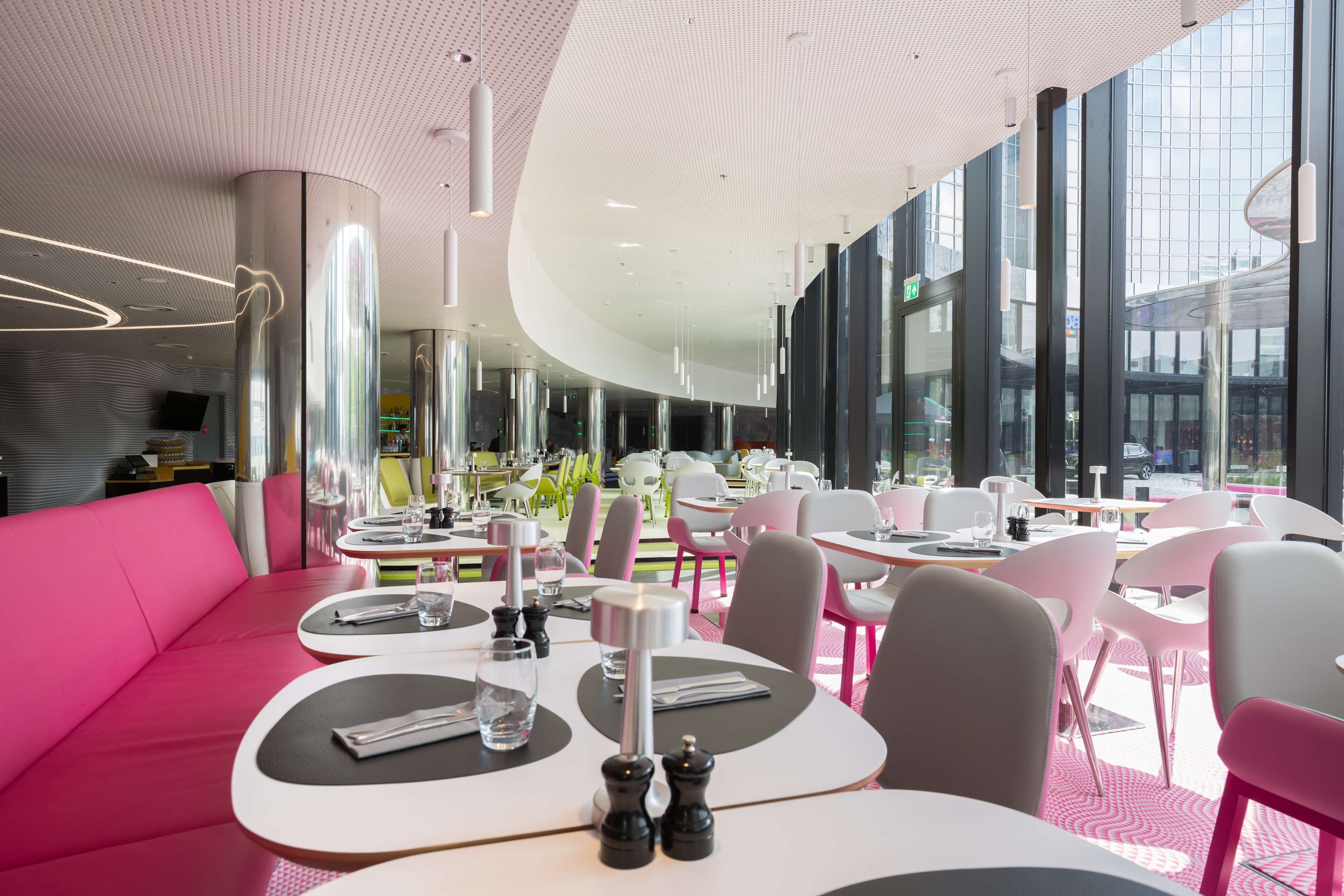 A modern restaurant with round tables, pink seating, and large windows offering views of the street.