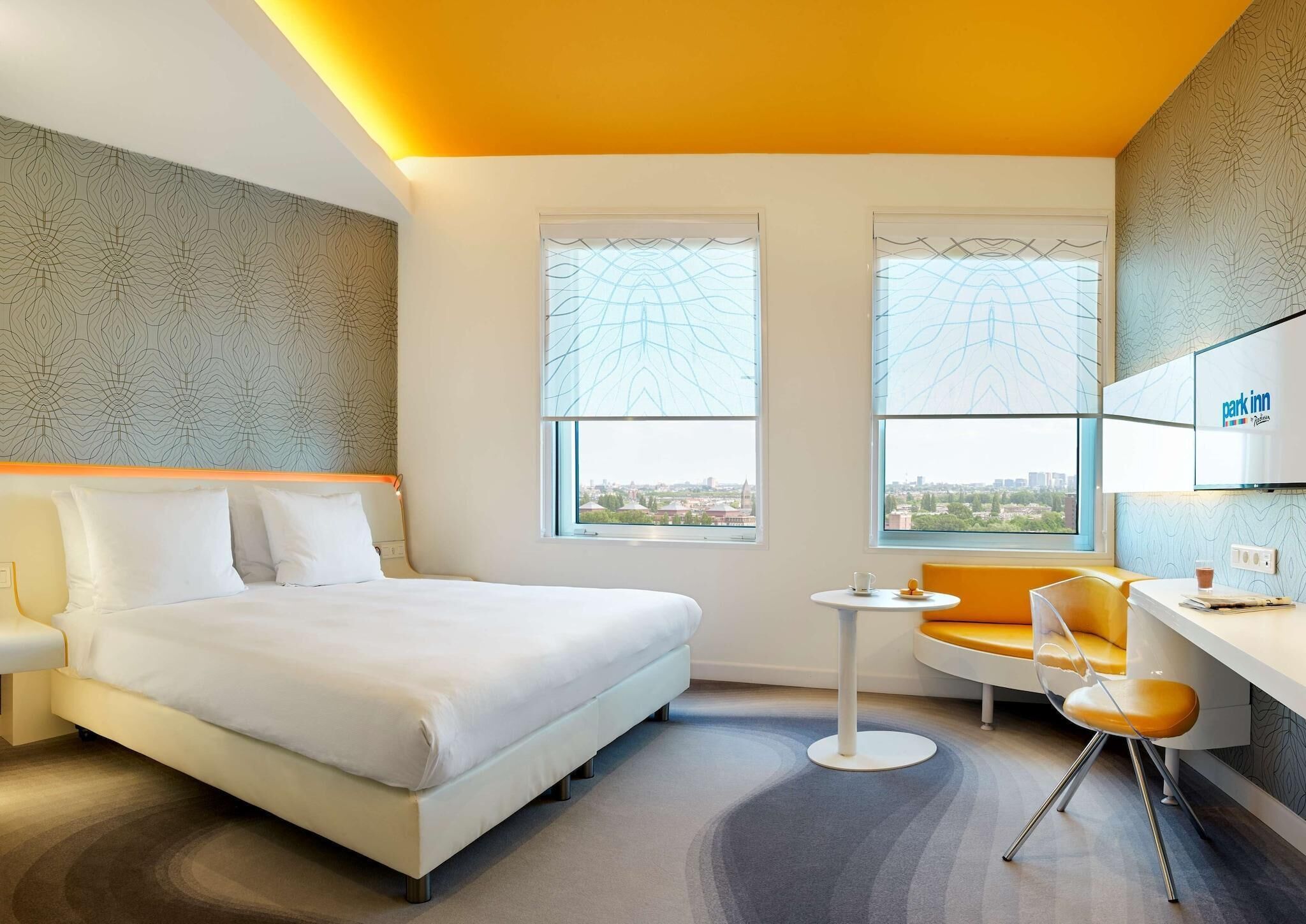 Une chambre d’hôtel équipée d’un lit, d’un bureau, d’une chaise, de deux fenêtres et offrant une vue sur la ville.
