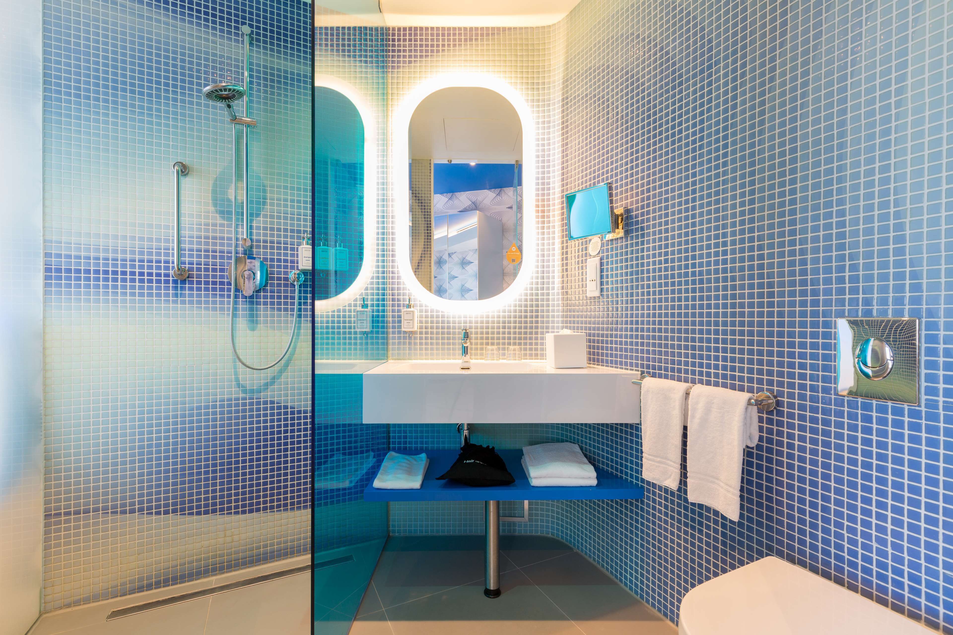 A bathroom with a blue tiled wall, a white sink, a mirror, a shower, and a toilet.