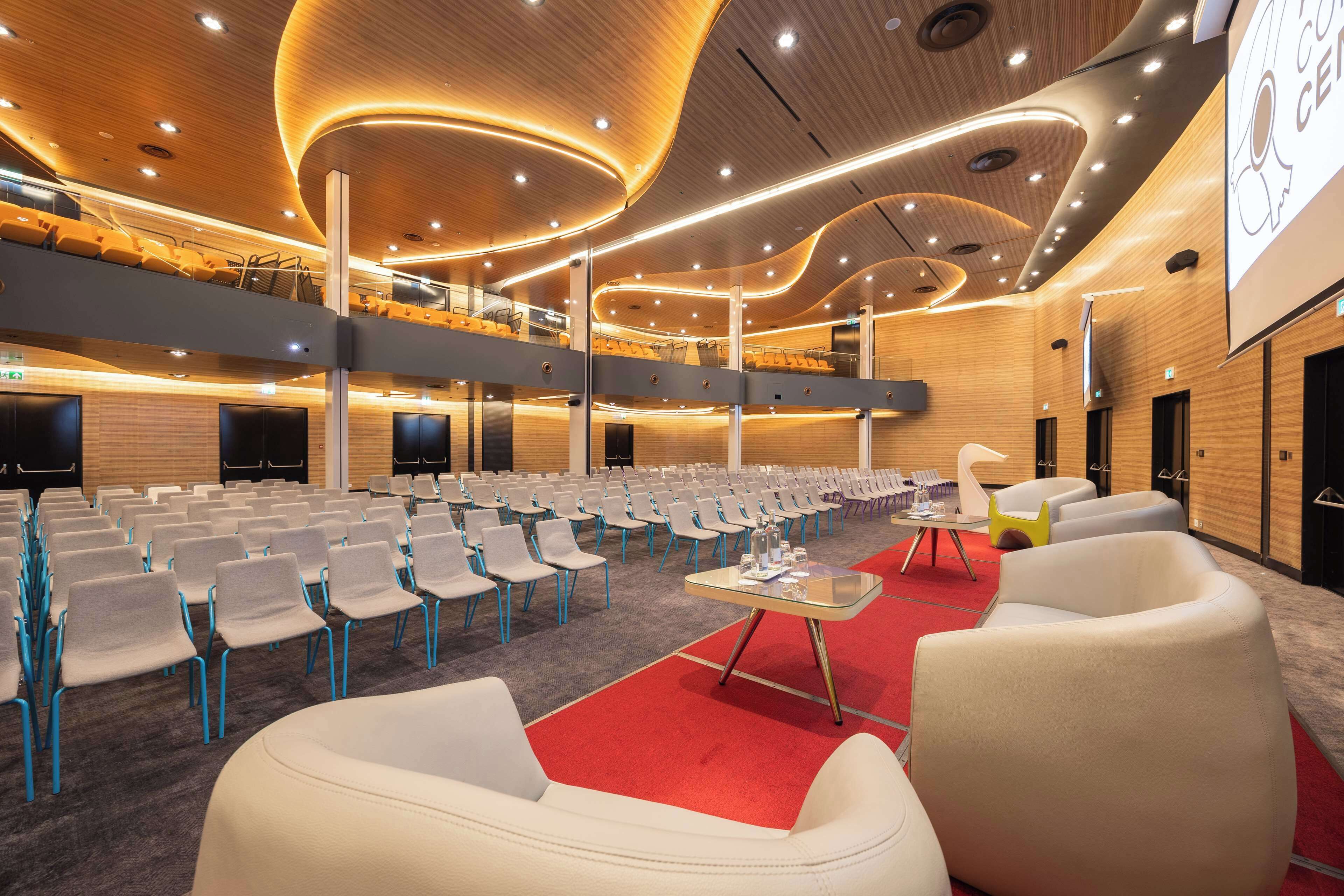 Una sala de conferències amb seients escalonats, una catifa vermella i un disseny de sostre modern.