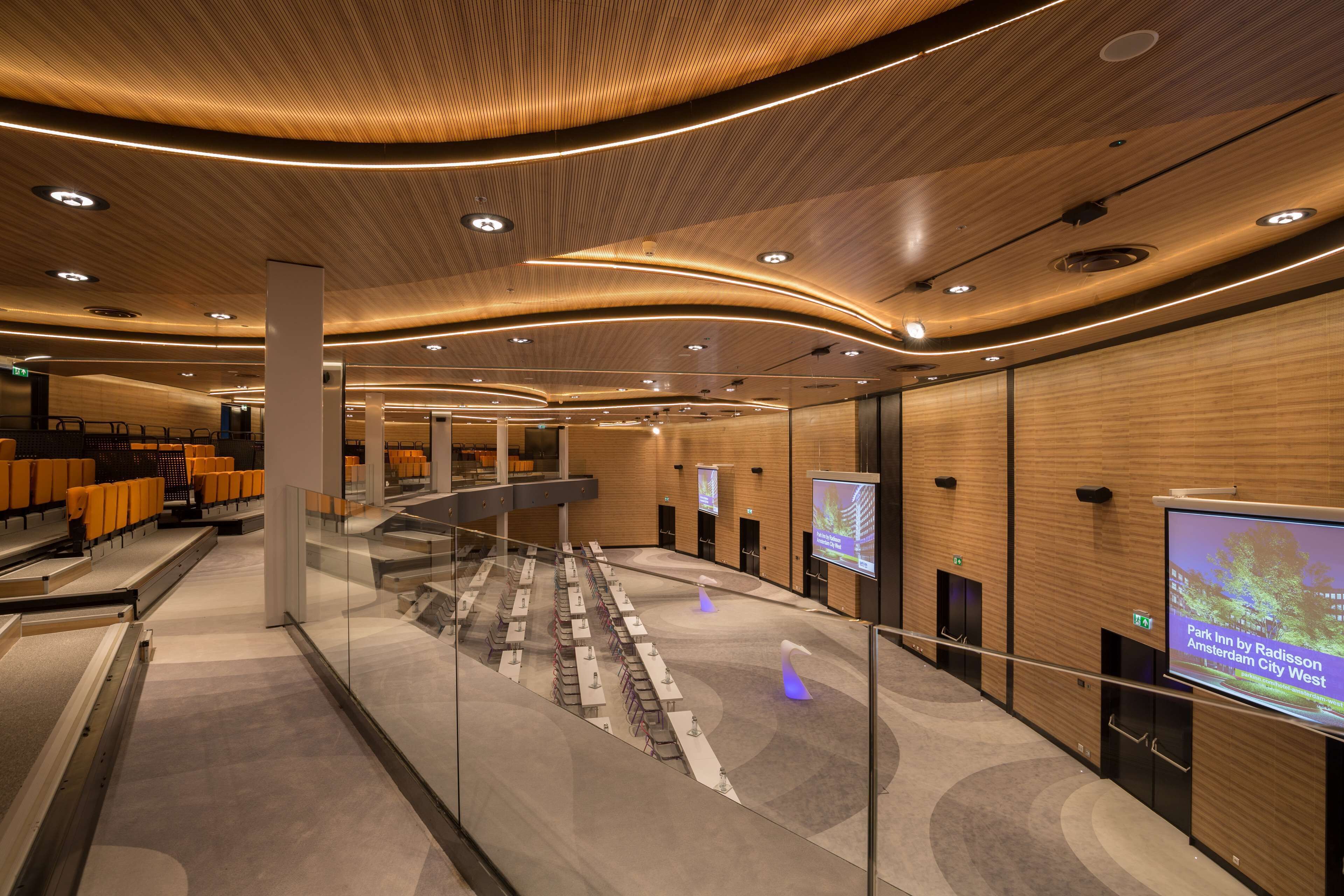 A modern hotel lobby with a curved ceiling, glass railings, and a central staircase.