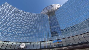 Un edificio moderno de vidrio con fachada curva y un logotipo visible en la parte inferior derecha.