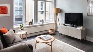 A modern living room with a sofa, a coffee table, a TV, and a large window. - Native Fenchurch  (London)