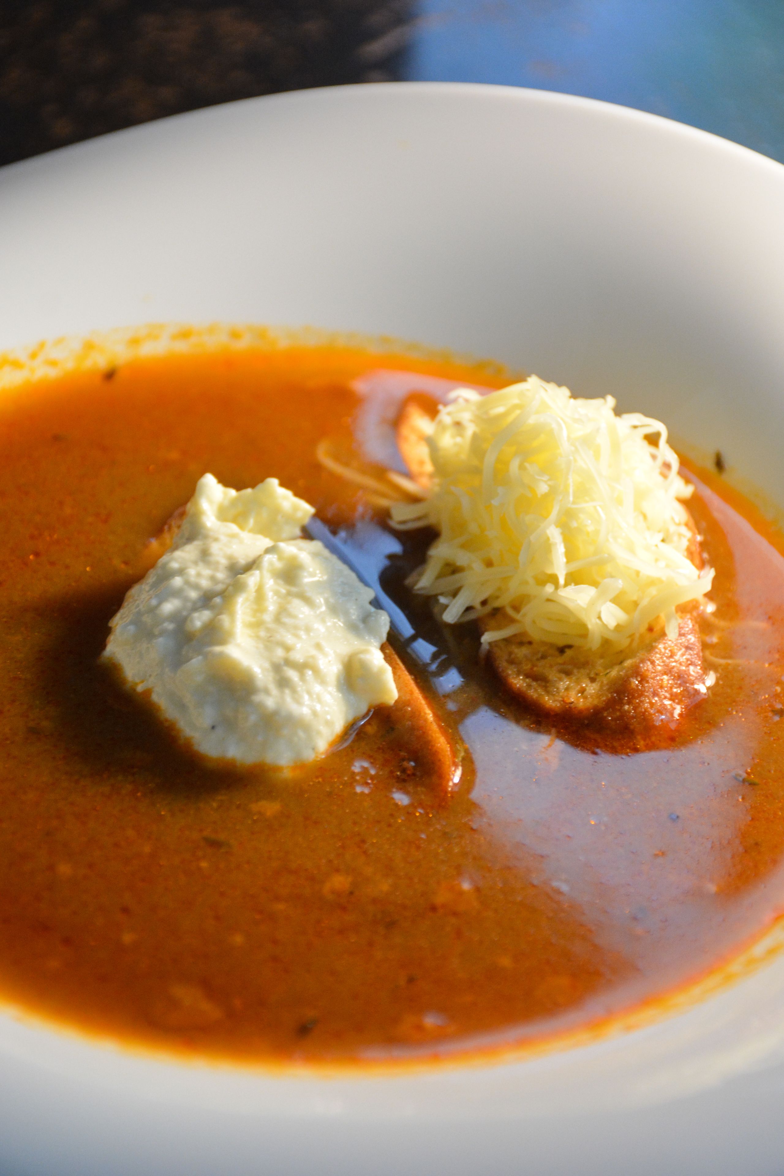 A bowl of soup with a slice of bread and a dollop of cream.