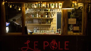 A bar with shelves of bottles and glasses, a neon sign reading "LE POLE", and a staircase in the background. - Le Pôle Résidence (Grand-Baie)