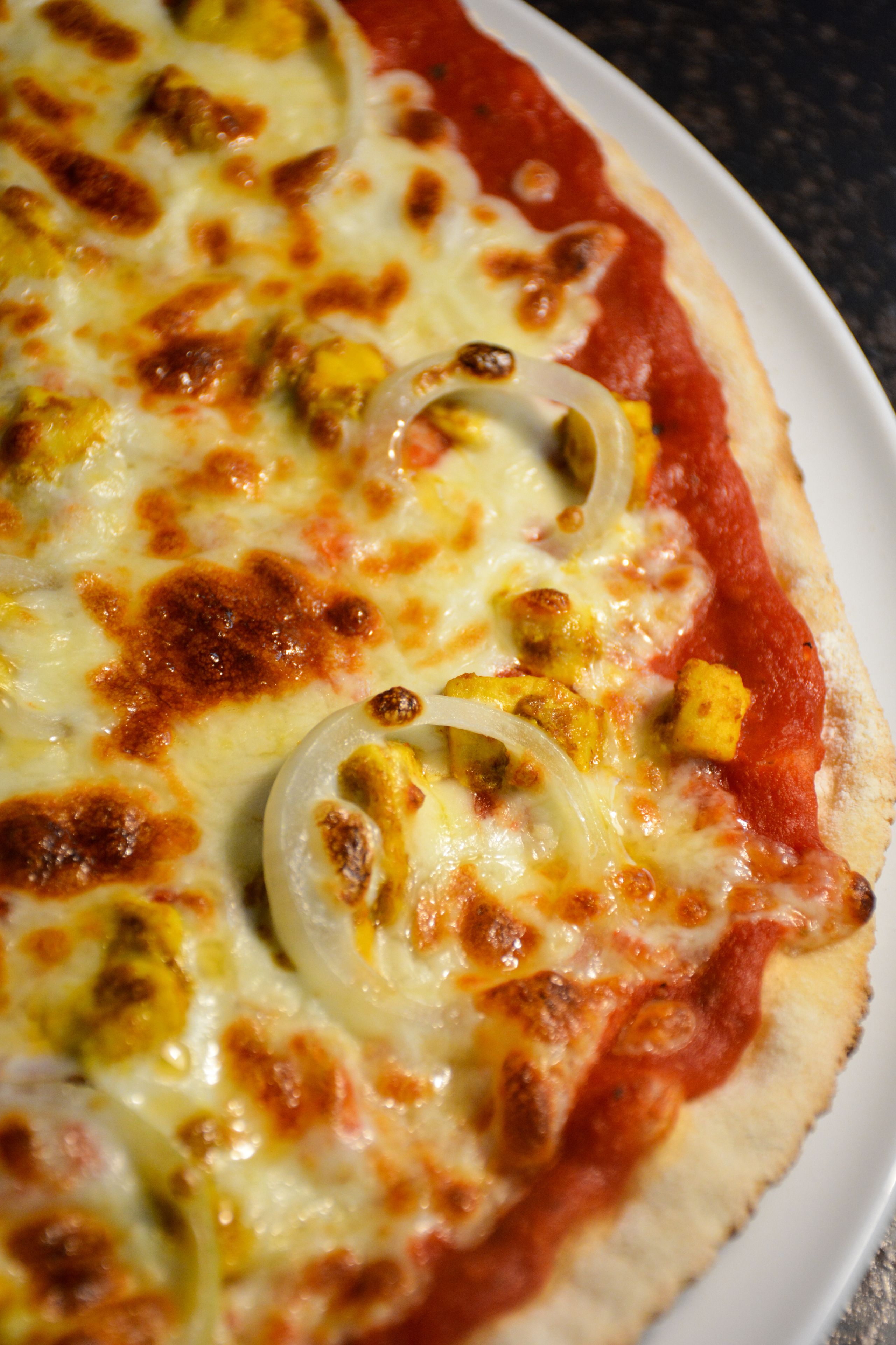 Una pizza con queso y cebollas sobre un plato blanco.