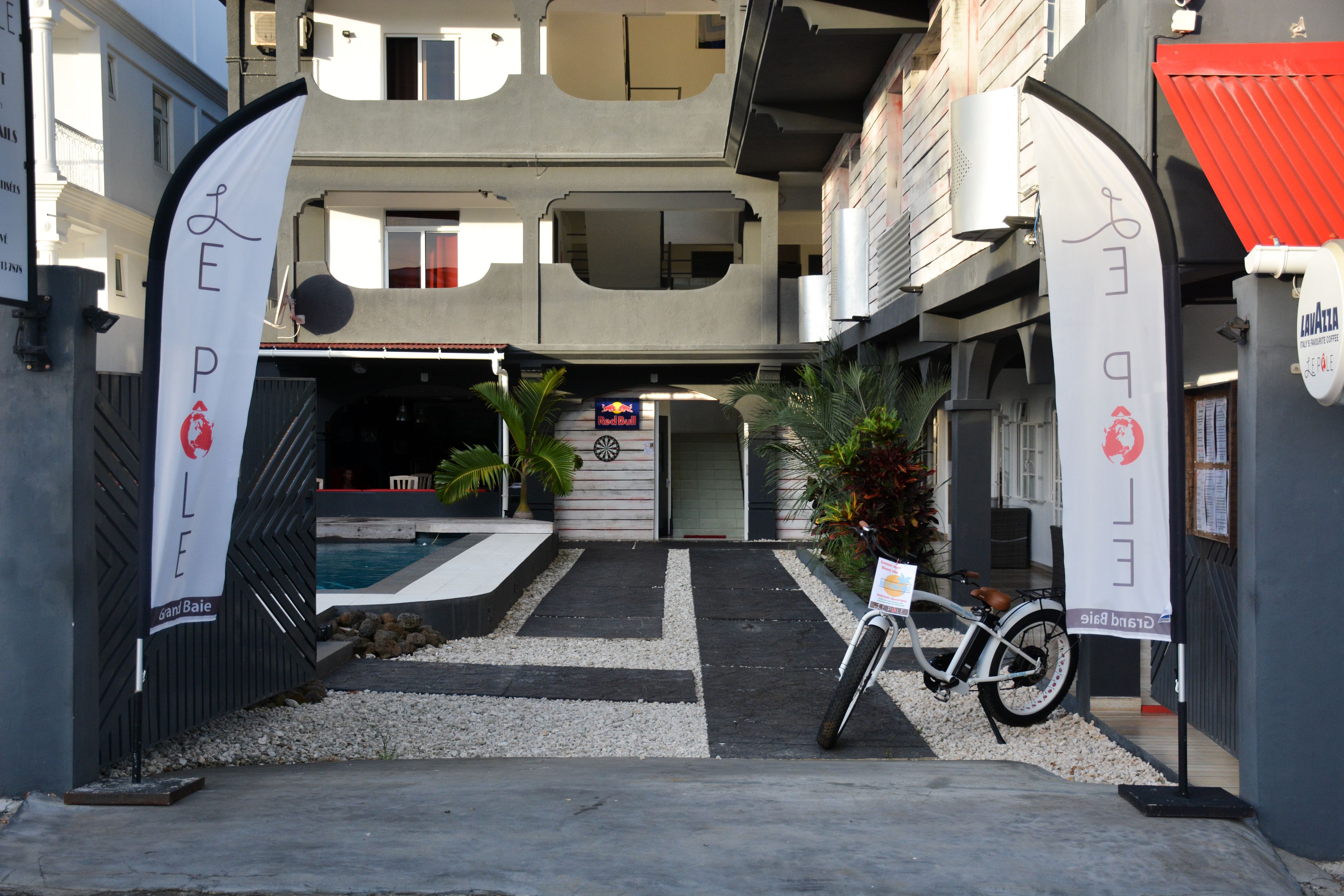 Ingresso di un edificio moderno con una bicicletta parcheggiata di fronte, una targa e, sullo sfondo, una zona piscina.