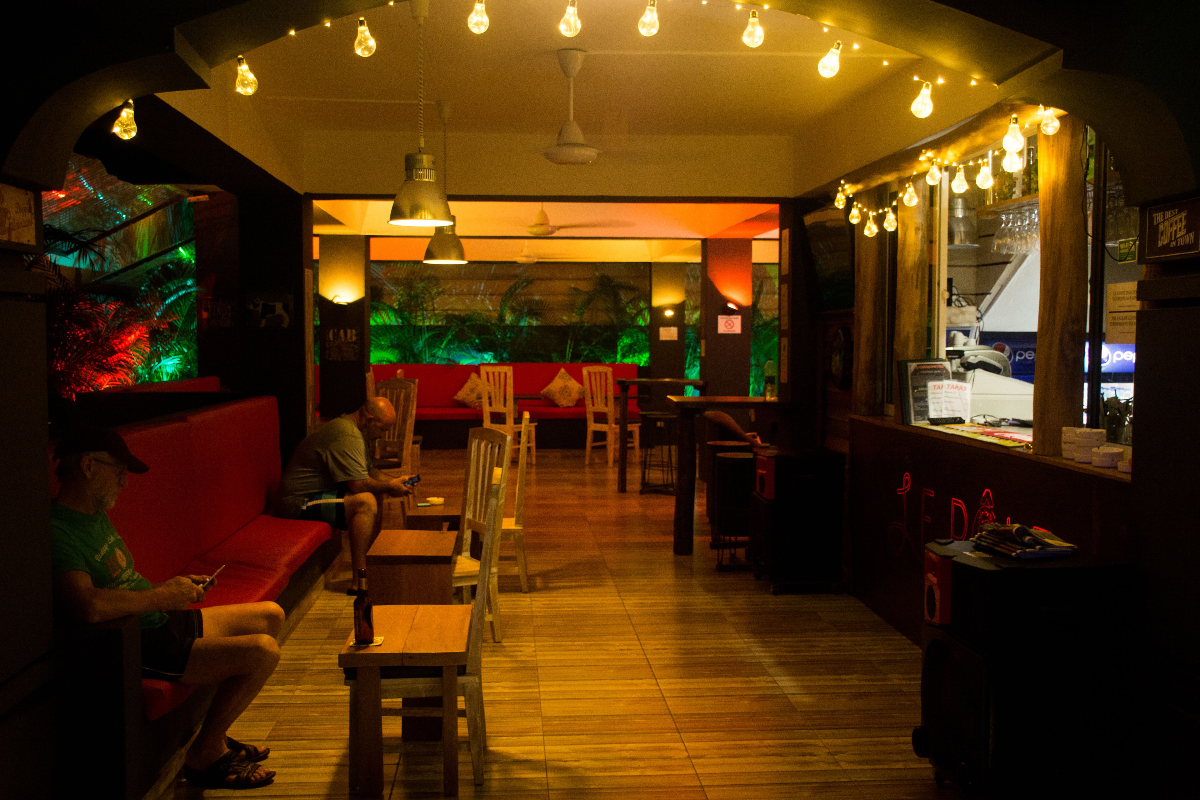 A dimly lit bar area with wooden furniture, a red couch, and a mural on the wall.