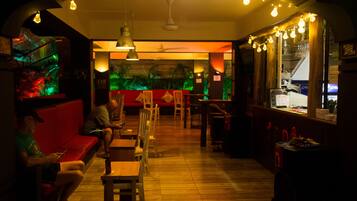 A dimly lit bar area with wooden furniture, a red couch, and a mural on the wall.