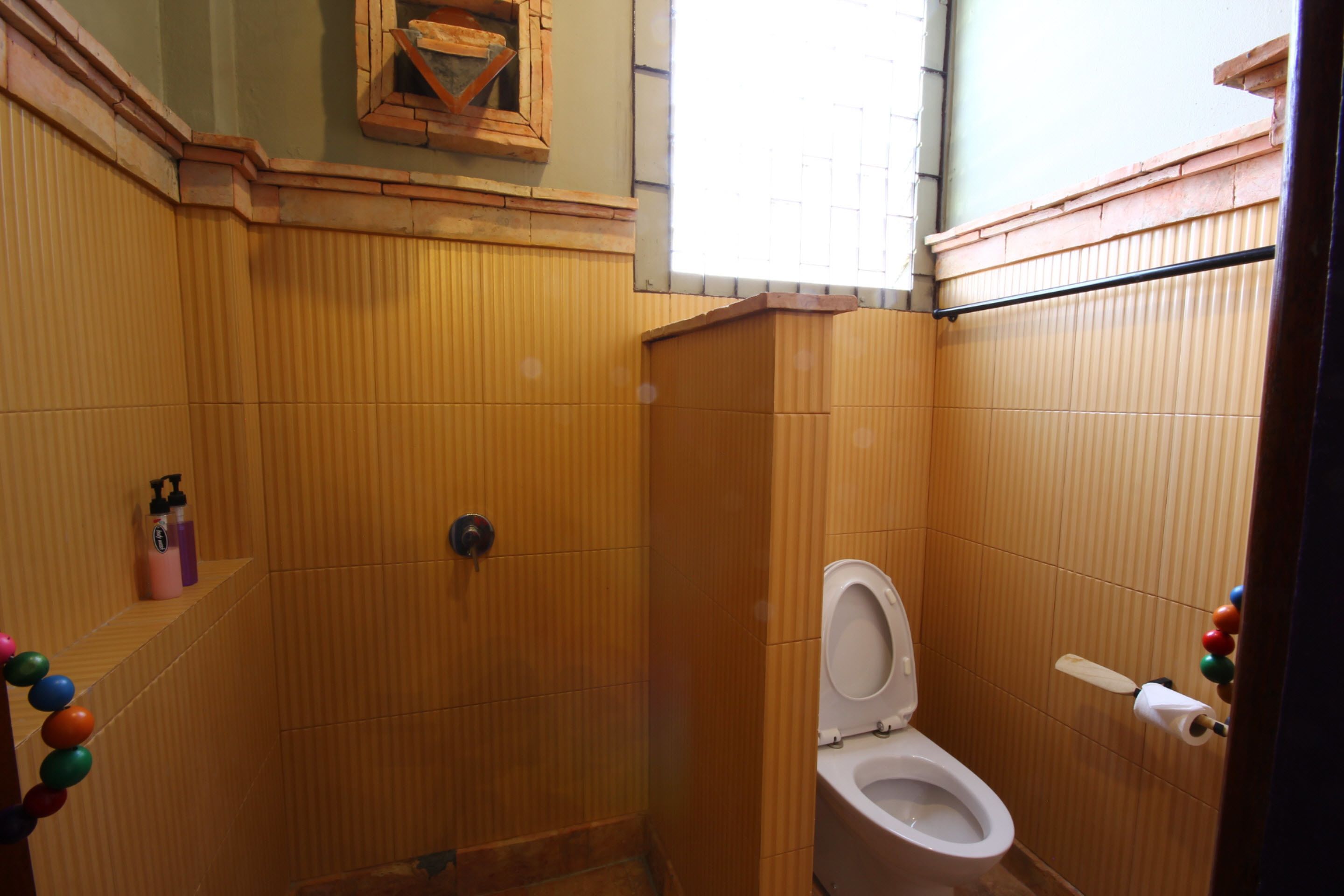 A bathroom with wooden paneling, a toilet, a shower, and a window.