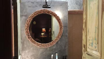 Un baño con espejo redondo, lavamanos circular y una lámpara colgante.