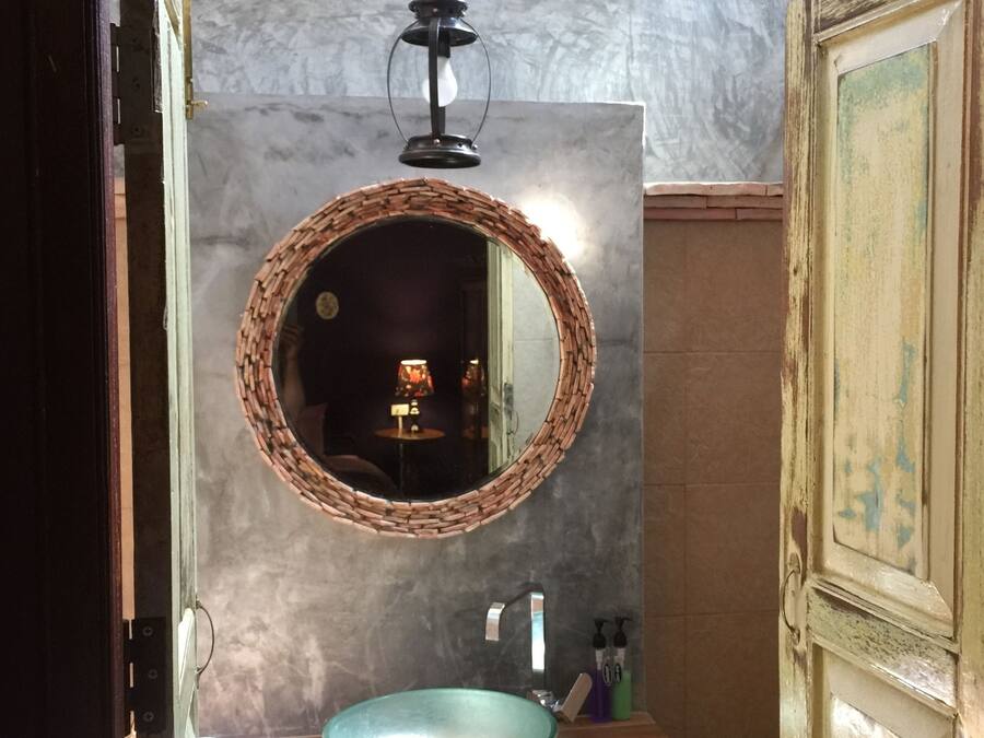 Un baño con espejo redondo, lavamanos circular y una lámpara colgante.