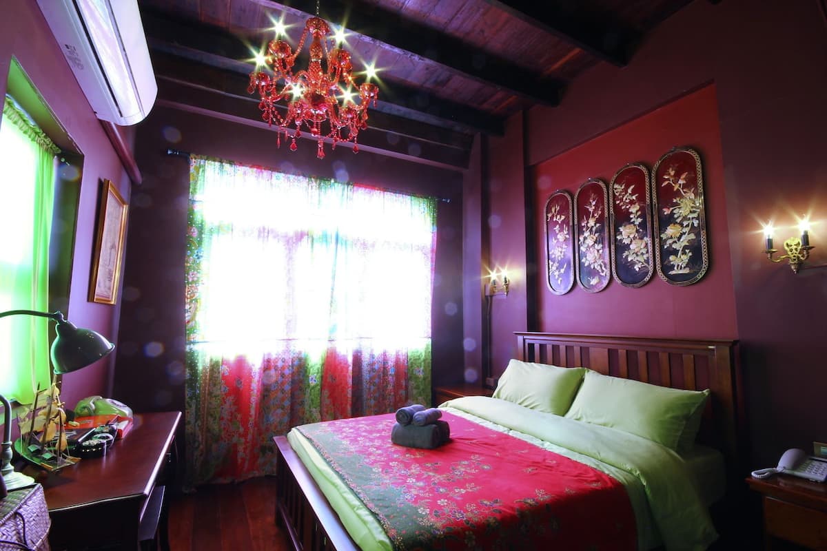 Ein Zimmer mit einem Bett, einer Chandelier, einem Schreibtisch mit Lampe und einem Fenster mit Vorhängen.