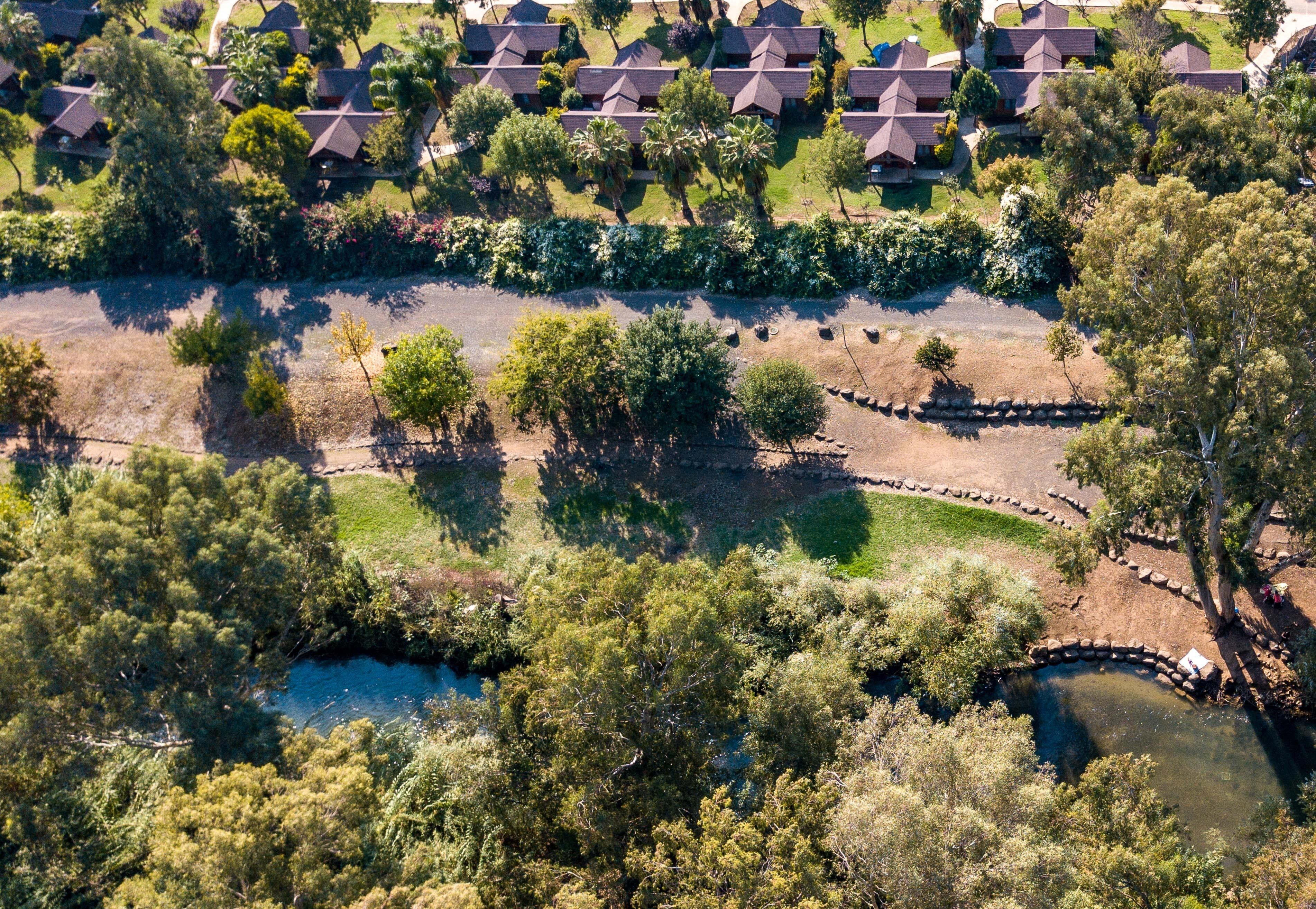 Vista aérea de um resort com vários edifícios no estilo de bangalôs, um lago central e vegetação exuberante ao redor.