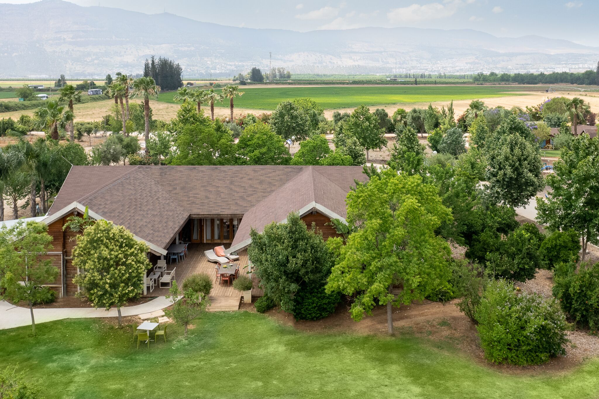 A large, single-story house with a sloped roof, surrounded by lush greenery and a well-maintained lawn.