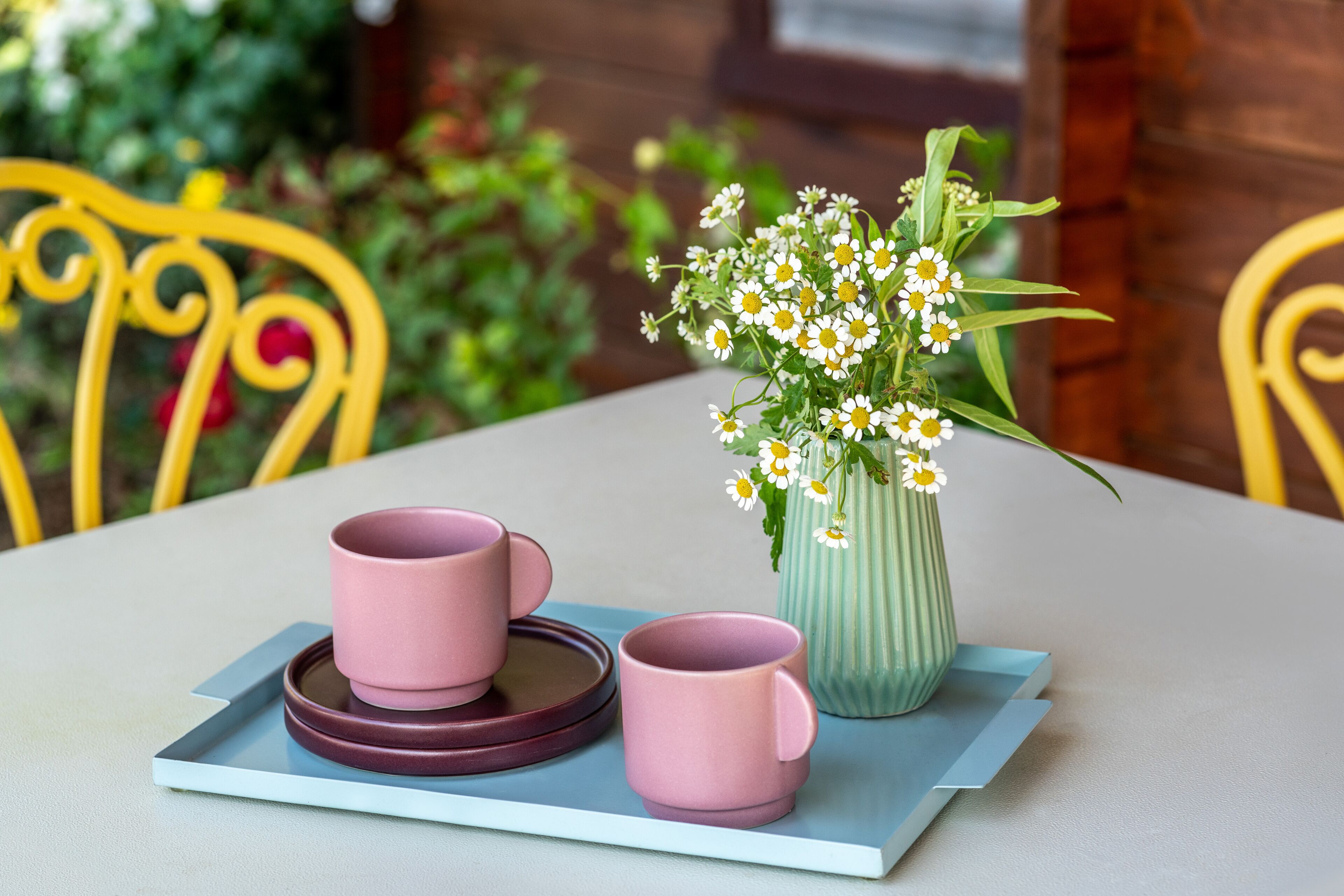 A table with two pink mugs and a vase with white flowers.