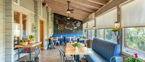 A restaurant with wooden ceiling beams, a chalkboard wall with menu items, and a large window offering a view of the outdoors.